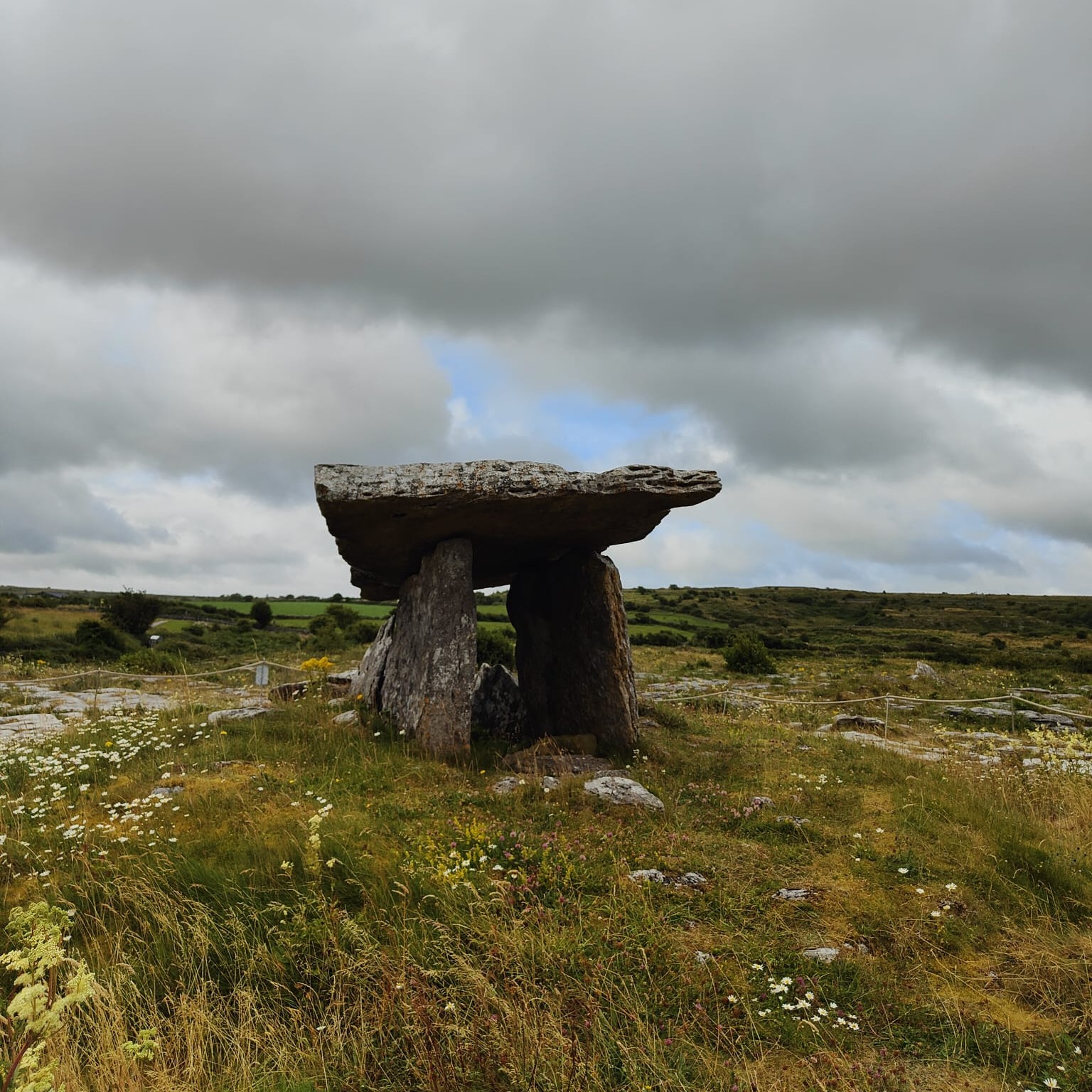 Did you know this slab of limestone has been standing here for over 5,000 years, older than the pyramids of Egypt?
This is a portal tomb, one of nearly 200 scattered across Ireland, but Poulnabrone is the oldest dated of them all. Neolithic farmers raised it sometime between 4200 and 2900 BC, hauling those two upright portal stones into place and balancing the huge capstone on top — no machinery, no metal tools, just people who wanted this spot to matter.
And it did matter. When archaeologists finally excavated beneath it in the 1980s, they found the remains of more than 30 people — men, women, children, even a Bronze Age infant buried here centuries later. Alongside the bones: a polished stone axehead, pendants carved from bone and quartz, pottery fragments.
As locals tell it, the tilt of the capstone was no accident. It's angled low at the back, and some say that was deliberate — a kind of doorway sloped just enough to help a soul slip more easily into the next world.
📍 Poulnabrone Dolmen, the Burren, Co. Clare
Visit the Burren