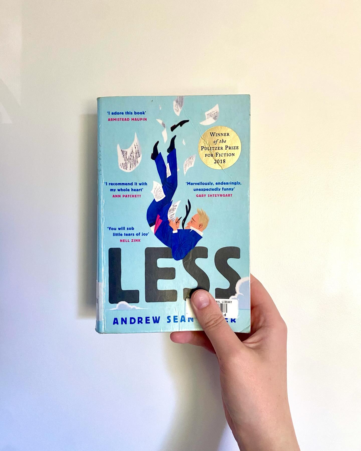 ‘Less’, Andrew Sean Greer
Who says you can’t run away from your problems?
Arthur Less is a failed novelist about to turn fifty when he receives an invitation to his ex-boyfriend’s wedding. He can’t say yes – it would be too awkward; he can’t say no – it would look like defeat. So, he begins to accept the invitations on his desk to half-baked literary events around the world. Anything to take him away from his ex’s wedding.
ID: a pale hand holding up the book ‘Less’ against a white wall.