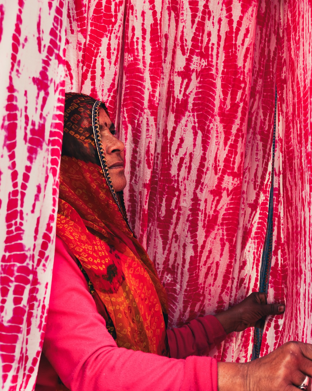 “Between Two Worlds” by Parboni Pallav Bose
In the desert air of Sangner, colour is everywhere, in vats, in cloth, in the wind. Known for its centuries-old dyeing traditions, this town near Jaipur has long been the beating heart of Rajasthan’s textile heritage.
“I captured this photograph in one of Sangner’s dye yards: a woman wearing the iconic Rajasthani tie-dye of Bandhani, photographed in the dye yard. She’s marked by tiny, constellation-like dots passed down through generations; each knot a memory, each pattern a prayer.
It was important to photograph these women because traditionally in Rajasthan, they spearhead the tying of the bandhani or leheriya, while the dying is done by the men. Fabrics always have a strong link with women, where skills & pieces of clothes are generationally passed down to be safeguarded.
Beyond that is a portrait of a woman, representing her role in cultural continuation and a perceivably male-dominated industry.
This photograph is copyrighted by Parboni Pallav Bose.
#theimpactsociety #textilesofindia #shiboristyle #bandhani #heritage #culture #storytelling #storyteller #textileindia #photography #visualstorytelling