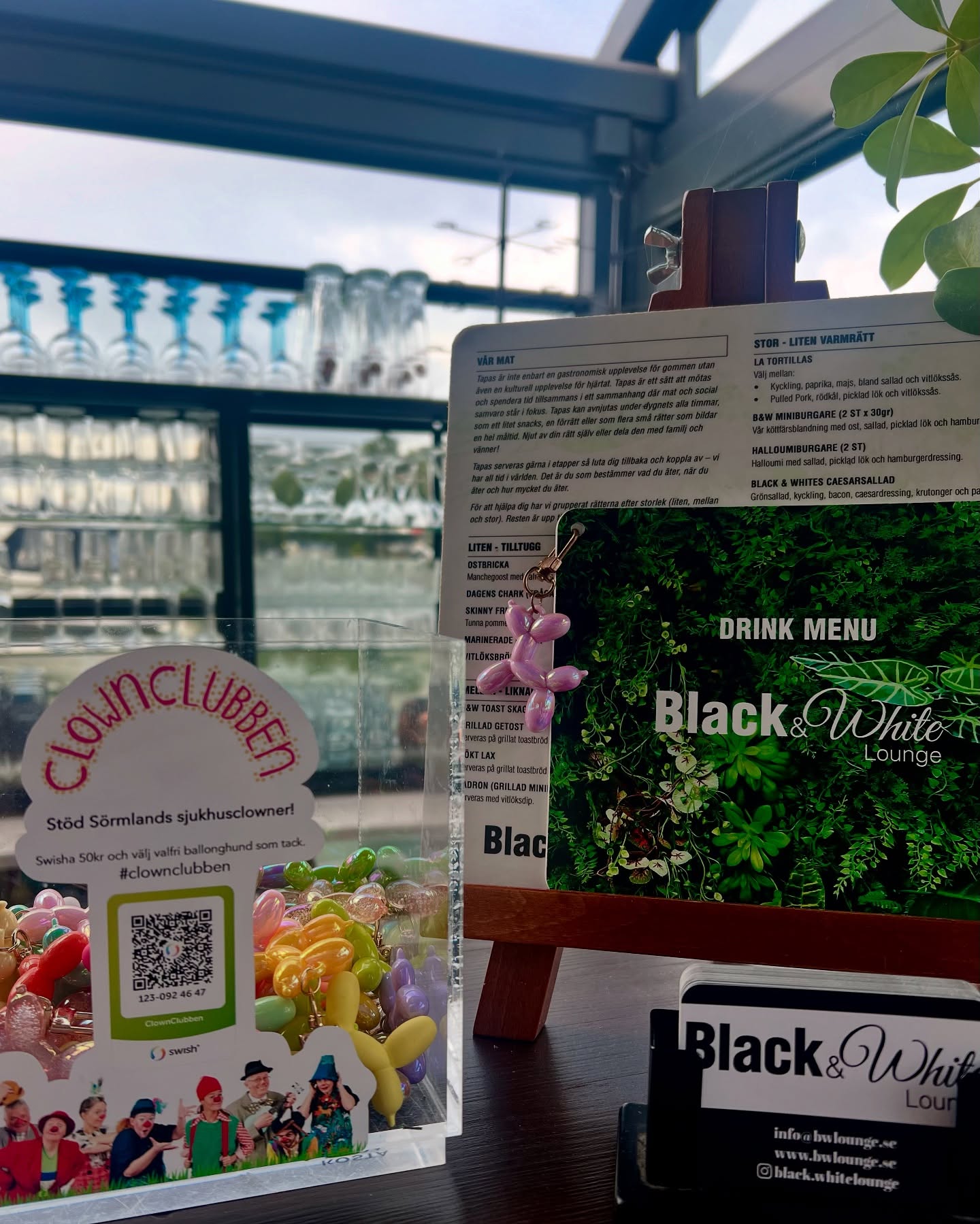 ClownClubben är Sörmlands sjukhusclowner och dem besöker framförallt barn på Mälarsjukhuset samt Nyköpings lasarett men dem gör även besök hos seniorer på demensboenden runt om i Sörmland.
Syftet är kort och gott att sprida glädje, lek och fantasi, till de som vill. Att hamna på sjukhus kan vara tufft och clownen blir ett kontrast och komplement till övriga vården.
Hos oss på Black & White Lounge hittar du deras färgglada ballonghundar – de sitter på våra menyer och många gäster har redan förälskat sig i dem.
Vill du ta med dig en hem? Swisha 50 kr till ClownClubben så är den din!