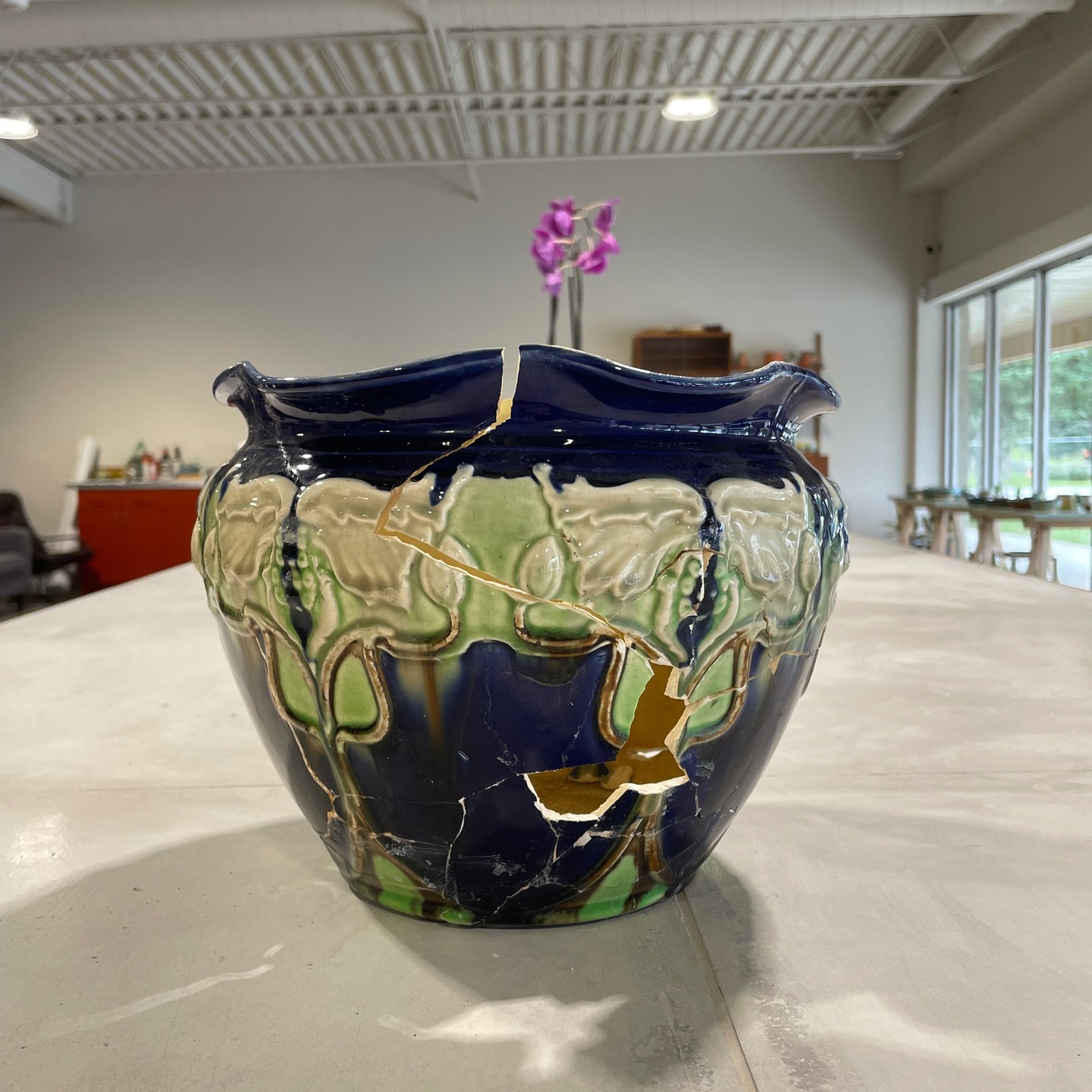 Crafting a Custom Creation
A client approached me with a truly unique piece, but it was in rough shape and needed some serious TLC. I knew I couldn’t fix the original, so I offered to do my best and replicate it instead.
Now, I'll be the first to admit that drawing isn't my strong suit—stick figures are about as fancy as it gets for me! But I dove in anyway. My first attempt was a bit of a miscalculation, and the piece came out on the smaller side. I decided to make the most of it and use it as a test pot to figure out the best way to add the intricate grape leaves and flowers.
Since my drawing skills are, well, nonexistent, I asked my partner, Peter—a talented artist—for help. I had the not-so-bright idea to try and pipe the design on with an icing bag. Turns out, it's not as easy as it looks! The clay was difficult to control, making a smooth finish impossible. Peter, a master woodworker by trade and new to working with clay, did an amazing job with what I gave him. Sorry about that, Peter! Thank you so much for all your help with this piece ❤️.
With a test pot now in hand and a new, larger pot thrown, I still needed to figure out how to get those delicate leaves and flowers onto the good pot. I had thought about casting the whole piece in the beginning, but it was missing too many sections and had been glued together with so much crazy glue that I worried it would fall apart.
With the clock ticking and the clay drying, I decided to take a chance and create a plaster mold of just one of the flower and leaf sections. I'm pretty sure I used an entire bag of clay just to fill the holes and prop up the original piece! Once the mold was ready, I used my slab roller to create six pieces of the same thickness, which we then pressed into the mold. After scoring, slipping, and blending each section, I had attached them to the new pot.
I've just finished glazing and firing the test pot, using three different glaze and wash combinations. The kiln is cooling down, and I can't wait to see how they turned out! Cheers Erin and Peter