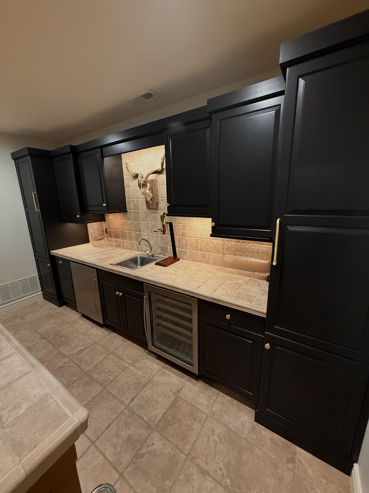 We painted this rustic basement bar in a custom dark bronze for a sleeker look. The homeowner finished it off with new gold handles, keeping the space masculine yet modern and perfectly in step with their transitional-rustic style.