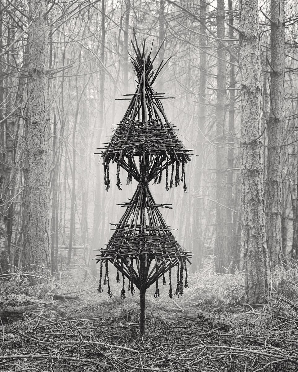 .
Introducing Jasper Goodall @jaspergoodall
-
His practice, whilst photographic, is rooted in the imaginary; using the natural landscape as source material spaces are altered either through the use of artificial light, physical intervention or reconstruction of natural elements to make a photograph. This alteration transforms real spaces into ‘make believe’ places.
Photography is a step in a broader process; often one involving the creation of physical objects or scenes that exist only temporarily. Their function is to serve as subject matter – props – for the finished image. This is not a documentary practice; it is more like imaginative image construction.
Goodall’s photography eschews the picturesque, instead reimagining the landscape as an eldritch narrative, exploring the tension between the beauty of the natural world and a sense that its mysteries have the potential to swallow us up. Each scene is an attempt to articulate stillness and solitude, whilst drawing attention to a sense of the quiet, abiding presence of the natural world.
-
This current body of work is Where once we stood a Scragged Oak Hill a project using the remnants of felled trees to build ‘forest figures.’ These talismanic forms act as a symbolic embodiment of the trees that have now gone – an arboreal haunting.
The Forest Figures draw, albeit indirectly, on older symbolic traditions—specifically animistic belief systems and European folk representations of nature. Figures such as the Green Man or the Woodwose embodied a personified, often unruly natural world – beings that blurred the boundary between human and landscape. While not literal depictions of these mythic forms, the Forest Figures can be understood as a contemporary reimagining of that impulse: to give shape to nature as an active, sentient force – they act as a witness to their surroundings.
The project’s title refers to the location of the first figure: Scragged Oak Hill, where a grove of mature hemlock trees once stood and were subsequently felled providing the catalyst and material for the first figure in this series.
#art #photography #woods #trees #marksoftheisles