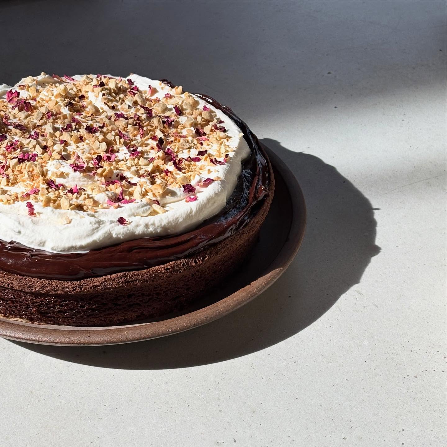 overheard that a client’s partner is celebrating a birthday and loves chocolate cake 👀 this is an olive oil chocolate cake with sour cream ganache and rose water whipped cream, topped with toasted cashews and rose petals ofc🥀