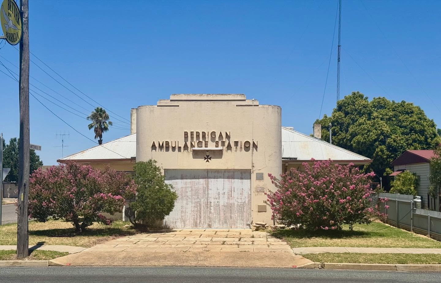 Rammed earth meets Moderne on Berrigan’s main street.
This former Ambulance Station was built in 1953 using pisé (rammed earth) on concrete foundations. It was designed by Riverina architect C. H. MacKnight, whose family were prolific experimenters with rammed earth construction across the region in the early-to-mid twentieth century.
In many 1950s country towns, especially those some distance from larger regional hospitals, ambulance stations—often community-funded and volunteer-staffed—were key pieces of health infrastructure. They provided organised transport, basic first aid, and a visible symbol of modern medical service, even though pre-hospital care was far less advanced and coverage far less uniform than today. More cars, longer distances and poor road-safety standards meant more, and often more serious, crashes.
The curved, symmetrical wing with its stepped parapet and incised ‘speedlines’ gives the building a distinctly Moderne profile, even though it is built with one of the oldest walling techniques around.
A fusion of ancient construction techniques and modernity in post-WWII rural NSW.
This is one of the places highlighted through Touring the Past’s newly completed Berrigan Heritage Review—a reminder of how inventive mid-twentieth-century country building and design could be.