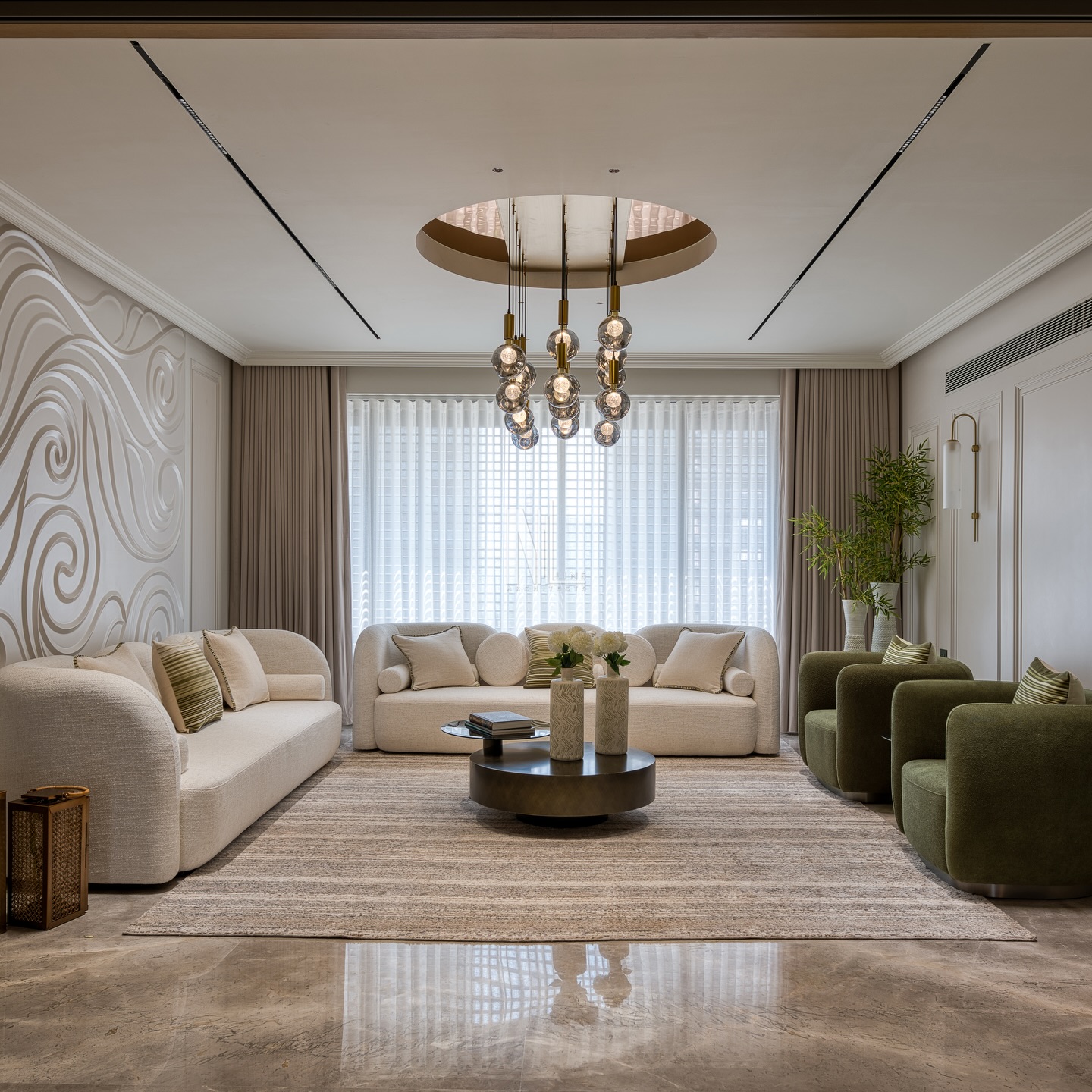 A formal living room crafted around soft curves and flowing geometry. The bespoke 3D CNC cut wall art sets the tone, bringing movement, depth, and an artistic tilt to the space. Paired with a curved sofa setup, plush green armchairs, and a circular chandelier echoed in the ceiling design, every element follows a harmonious visual rhythm.
Muted moulding panels on the right balance the drama with quiet elegance, styled with minimal wall lights that add warmth without distraction. A textured rug anchors the entire palette, tying together form, flow, and function into a serene yet sophisticated living experience.
✨ Timeless textures. Sculptural details. Soft luxury.