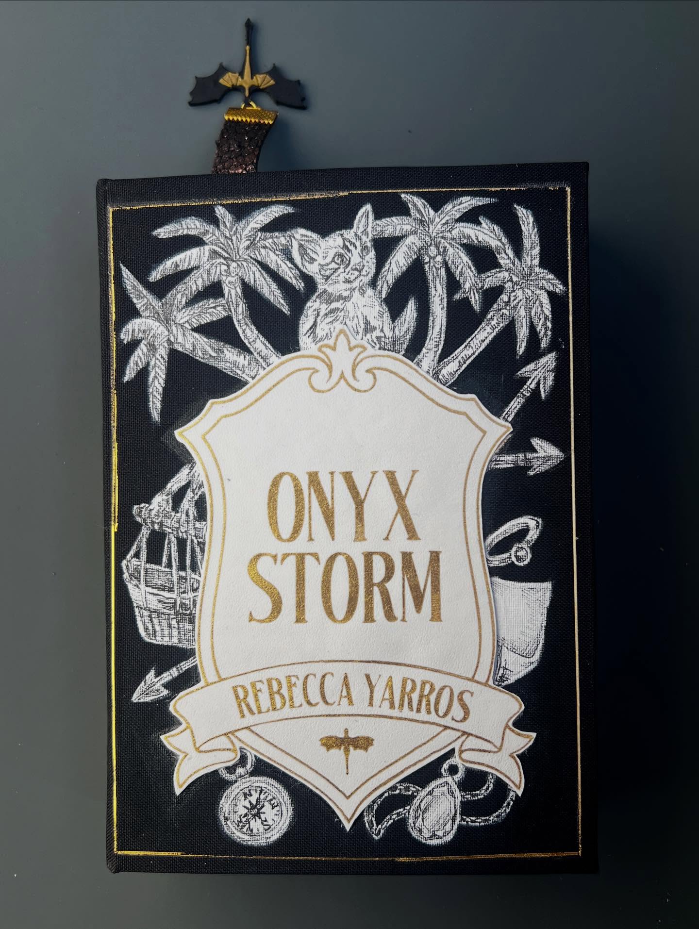 Full breakdown for the Onyx Storm rebind, 🚨🚨🚨 spoilers abound!
01. The cover of each of these books features a simple shield with the title and author name surrounded by illustrations of prominent characters and scenes from the book. Fans will notice the gifts from the Quest Squad’s journey like the compass and Broccoli (@_meganslattery_ sure noticed quick), the prince’s wee little basket, and a certain ring to name a few.
02. Video pulling all the elements together. The major themes of this book were a lot of travel and venin/wyvern fighting.
03. The big portrait for this book goes to Sgaeyl. What a little secret keeper. What a sneaky snake in the shadows.
04. The fore-edge gouache painting for this book features the big showdown between Violet and the big showdown in the final chapters, with collapses columns and the onyx storm of destruction.
05. “You will choose everyone over yourself and he will choose you over everyone.” is the quote I emblazoned in gold ink lightning over the metallic, storm cloud endpapers I printed myself.
06. The spines are all meant to imitate textbooks that would be on a shelf at Basgiath.
07. Another shot of Sgaeyl emerging from the shadows.