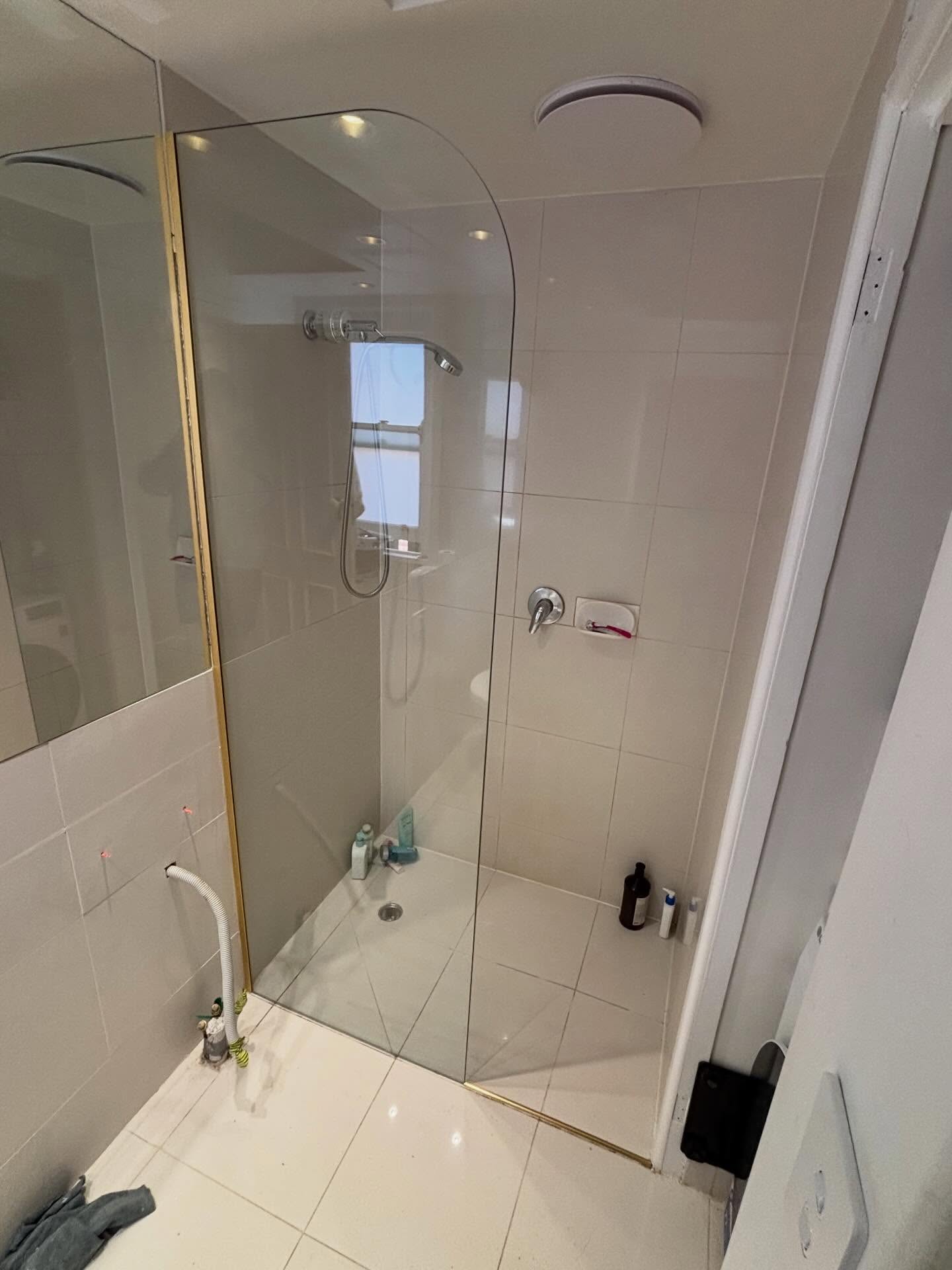 Custom radius frameless panel installed today in Toorak using a brushed gold wall channel.