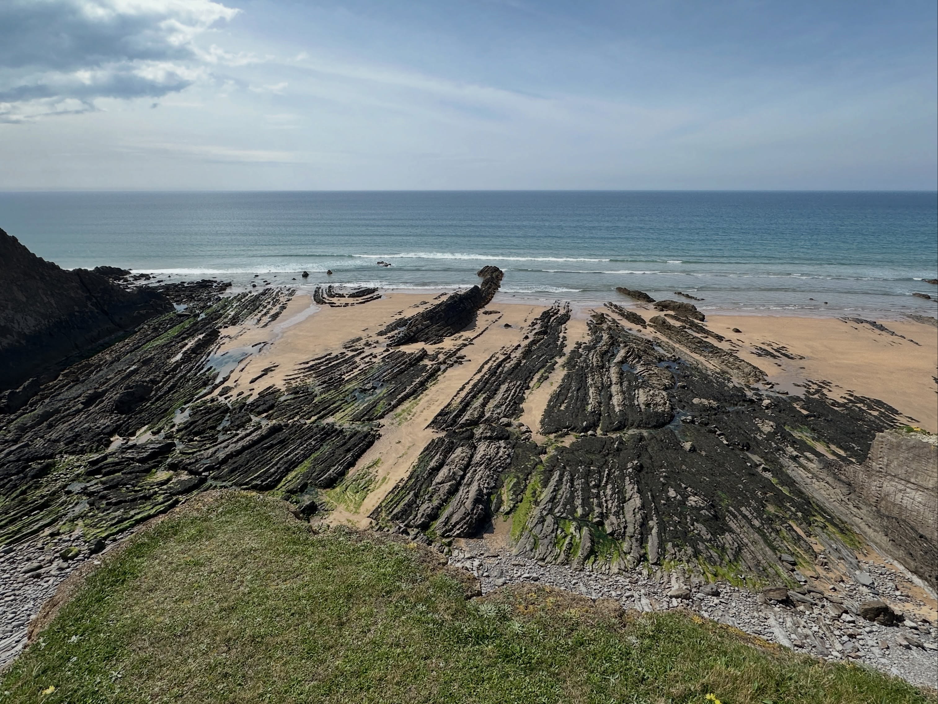 Incredible structural geology at Northcott Mouth in north Cornwall.
Here a series of large-scale upright antiform and synform folds are exposed in the foreshore, elucidating impressive deformation of these Carboniferous rocks during the Variscan Orogeny.
For those who might not be aware, structural geology is the study of structures in rocks that might give us some indication of how those rocks formed or the journey they have been on. Personally, I think one of the hardest sub-disciplines in geology.
These could be structures that form during sedimentary or igneous processes, but more often are structures that formed as a consequence of stresses that originate from tectonic processes in the Earth’s crust.
These structures provide a record of how rocks have deformed during their history, uncovering a story of tectonic processes through time.
Nowhere is this on display quite as majestically as in north Cornwall. It is structural geology heaven.
These originally horizontal layers of sedimentary rock were deposited as sediment gravity flows in the Culm Basin around 320 million years ago in the Carboniferous.
Crustal shortening during Variscan convergence caused these sedimentary basins to concertina together like an accordion. Their stratified sedimentary contents got squeezed and buckled, in doing so forming these beautiful structures.
The fact the trace of bedding appears to create these massive zigzag shapes in the horizontal foreshore platform tells us the fold hinges are plunging.
Because the antiform fold limbs converge and synform fold limbs diverge in a westerly (seaward) direction it tells us the folds are plunging towards the west.
You can also make out different fold hinge geometries, meaning there must be different strain rates and rheological contrasts in the rocks as well.
We use the term hinge for where the two fold limbs meet; where the bedding surface has buckled if you like. Think of it like the hinge of a door or the spine of a book.
A tectonic story well worth seeing!
#cornwall #geology #structuralgeology #geologist #geologyrocks