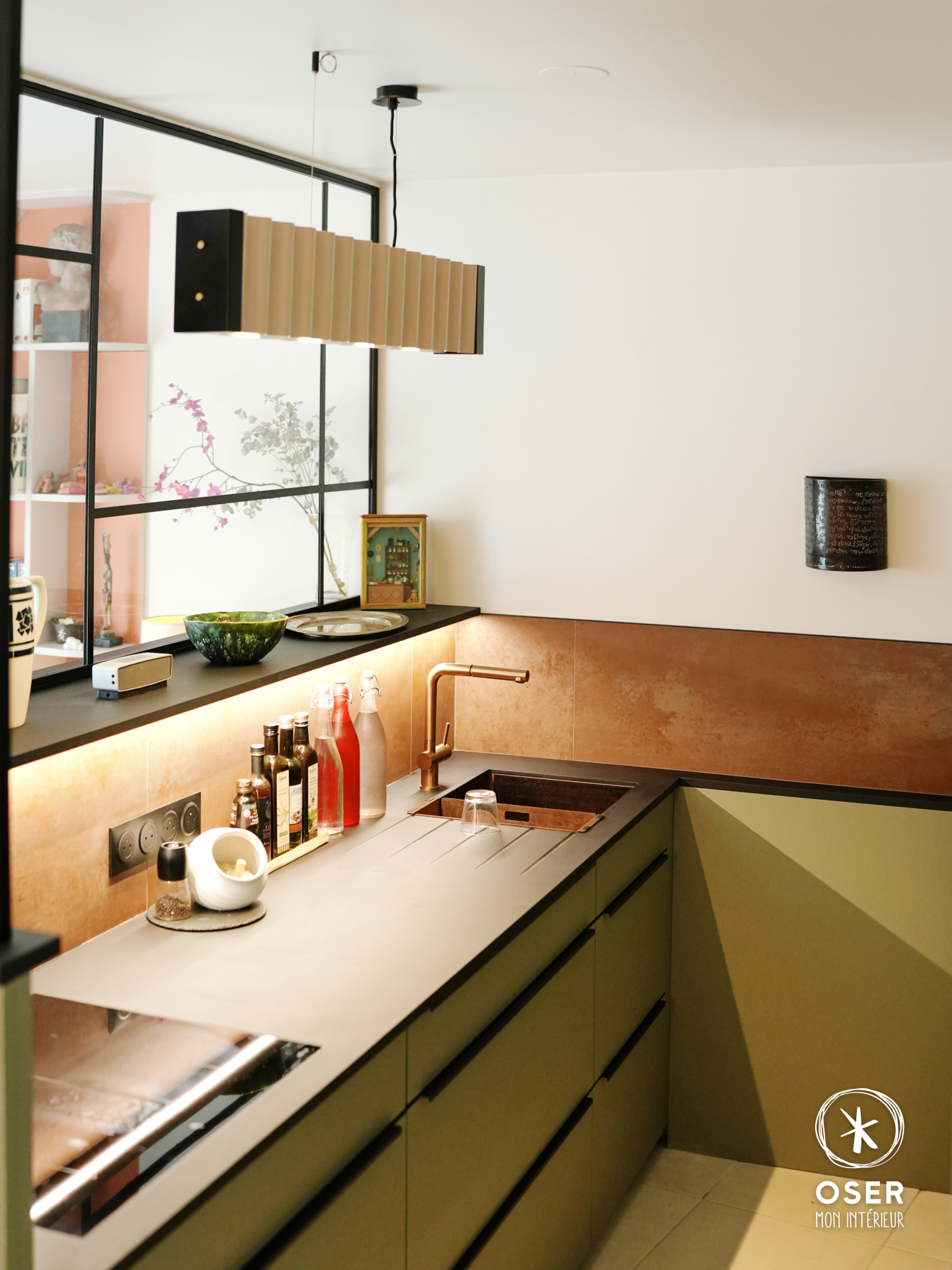 Un cube dans un cube. Un parti pris fort pour ce projet à Bruz.
La cuisine ? Elle ne longe plus un mur. Elle devient un volume. Un bloc compact, graphique, autonome ; délimité par une verrière à plat noirs qui sépare sans cloisonner, et qui laissent passer la lumière depuis le salon.
Côté matériaux, on a joué la cohérence des contrastes :
→ Façades vert sauge mat aux poignées profilées noires
→ Crédence effet métal rouillé, éclairée en bandeau LED
→ Mitigeur cuivré brossé en total look
→ Électroménager encastré, noir absolu
→ Luminaire ondulé, qui sculpture autant qu’il sert de source de lumière
En face, la salle à manger adopte le même langage : table ovale en chêne, chaises dépareillées (vert émeraude & écru), papier peint panoramique tropical. Une cohérence colorielle qui traverse tout l'appartement ; de la bibliothèque orangée au mobilier TV vert d'eau.
Nous avons eu le plaisir d’accompagner nos clients dans le but de transformer cette appartement fraîchement livré en quelque chose qui leur ressemble.
Verrière @goude_glass
Papier peint @lesdominotiers,
Électricité (Thomas Jan),
Faïence (@esprit.casa.rennes),
Peinture (Mat Color)
Agencement bibliothèque sur mesure Domelia.
@nobilia_de @aromasdelcampo
🏠 Projet : appartement neuf à Bruz (35)
📐 Mission : conception et suivi complet
📸 Résultat : un intérieur qui ne ressemble à aucun autre
📩 Vous avez un projet de rénovation ? Parlons-en.
-------
OSER MON INTERIEUR, cabinet d'architecture d’intérieur et de maitrise d'oeuvre, pour professionnels et particuliers.
-------
©️ Photo & Vidéo : 📸 @size_up.io
#architecteinterieur #agencement #maitrisedoeuvre #Rennes