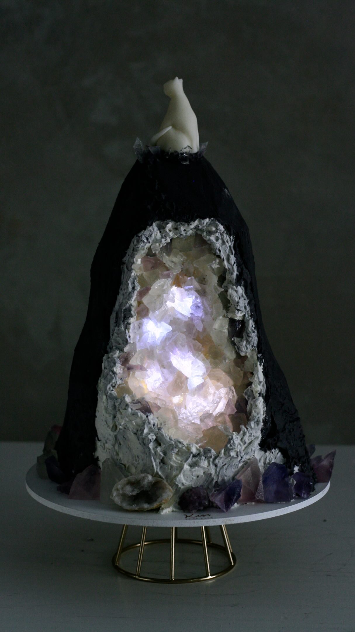 GEODA VIVA: Blue Moon Birthday Cake
Some projects begin with a design brief.
Others begin with an idea.
For this piece, the inspiration came from a love of crystals, lunar symbolism, cats, and the quiet beauty hidden within nature.
Rather than recreating a geode literally, I wanted to capture the feeling of discovering light inside something that appears dark and solid from the outside.
The crystal chamber was built using edible Kohakutou crystals, chosen for their ability to catch and reflect light. A hidden illumination within the cave transforms the piece throughout the evening, creating subtle shifts of colour and depth.
The exterior was sculpted in obsidian black, while a white cat sits above as a silent guardian.
What fascinated me most about this project was the contrast:
Darkness and light.
Strength and fragility.
What is visible and what remains hidden.
GEODA VIVA.
A living geode interpreted in cake.
#ibizaluxury #ibizabirthday #cake #geodecake