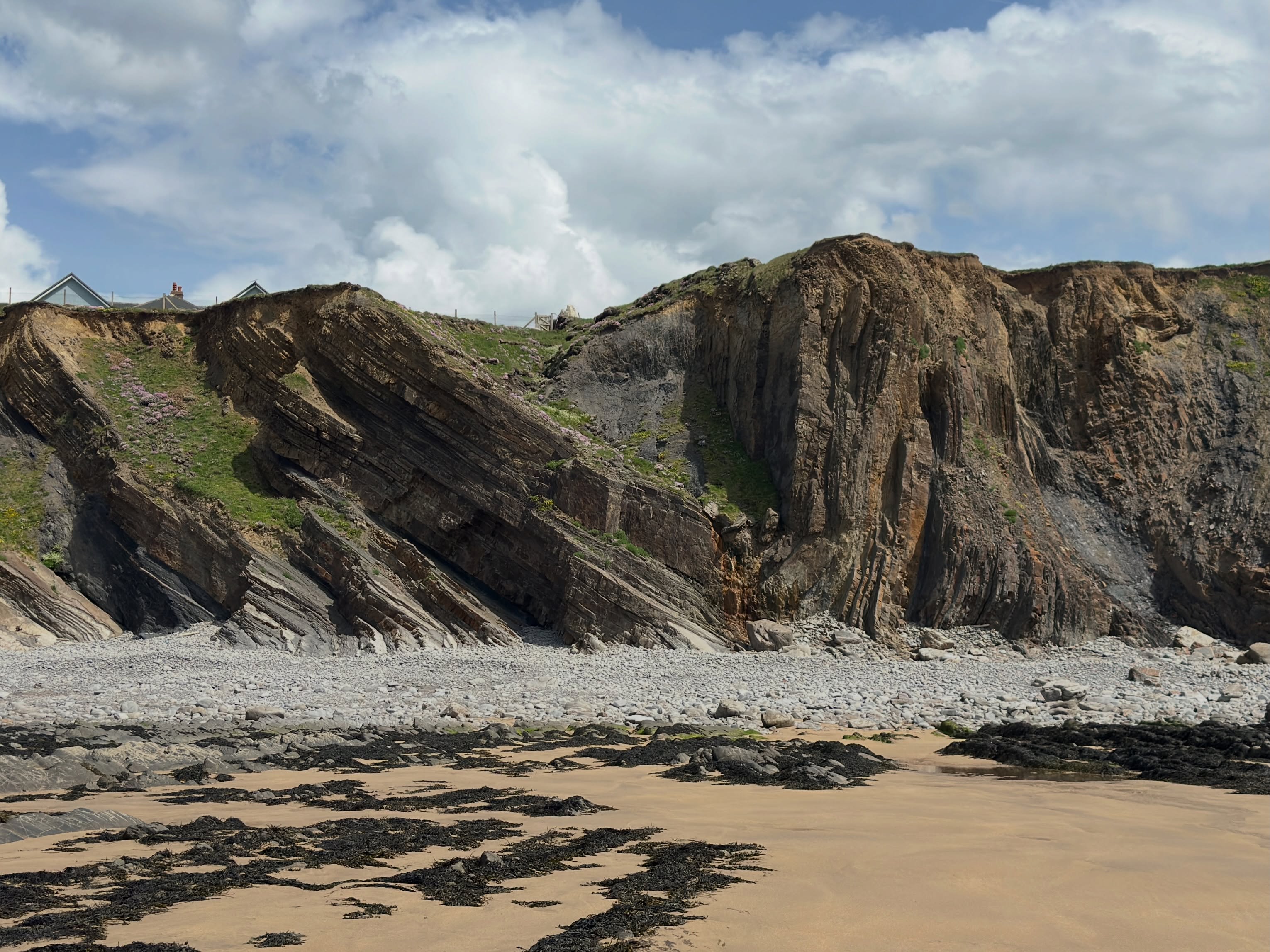 Here’s a “what a geologist sees” post for a section of the incredible cliffs at Northcott Mouth Beach in north Cornwall.
To be honest, you really don’t need an annotated image to highlight what’s going on here. It’s so big and in your face! I’ve done it anyway though, just because I enjoy doodling over the photos. It’s very therapeutic.
Here’s some info as to what’s going on. In this image you can see a large-scale, northwards-verging synform fold, elucidating impressive deformation of these Carboniferous rocks during the Variscan Orogeny.
These originally horizontal layers of sedimentary rock were deposited as sediment gravity flows in the Culm Basin around 320 million years ago in the Carboniferous.
Crustal shortening during Variscan convergence caused these sedimentary basins to concertina together like an accordion. Their stratified sedimentary contents got squeezed and buckled, in doing so forming these beautiful structures.
This fold is slightly inclined towards the north. In other words, if you join all the hinge points the line it creates (the fold axial trace) is tipping towards the north.
We use the term hinge for where the two fold limbs meet; where the bedding surface has buckled if you like. Think of it like the hinge of a door or the spine of a book.
For folds to form these rocks must have undergone some sort of shear, a type of deformation experienced by a rock mass. There are two types of shear - pure and simple.
Using the “cloth on a table” analogy, if you pushed a cloth together equally from both sides it would cause it to buckle as a series of upright folds. This is pure shear.
If you move your hand along the top of the cloth it would cause it to “ruck” over. These rucks tilt in the direction of the top sense of shear, the direction you move your hand in. This is simple shear.
Many folds in Cornwall have a top sense of sheer to the north - Variscan convergence had a northward direction.
A tectonic story well worth seeing!
#cornwall #geology #structuralgeology #geologist #geologyrocks