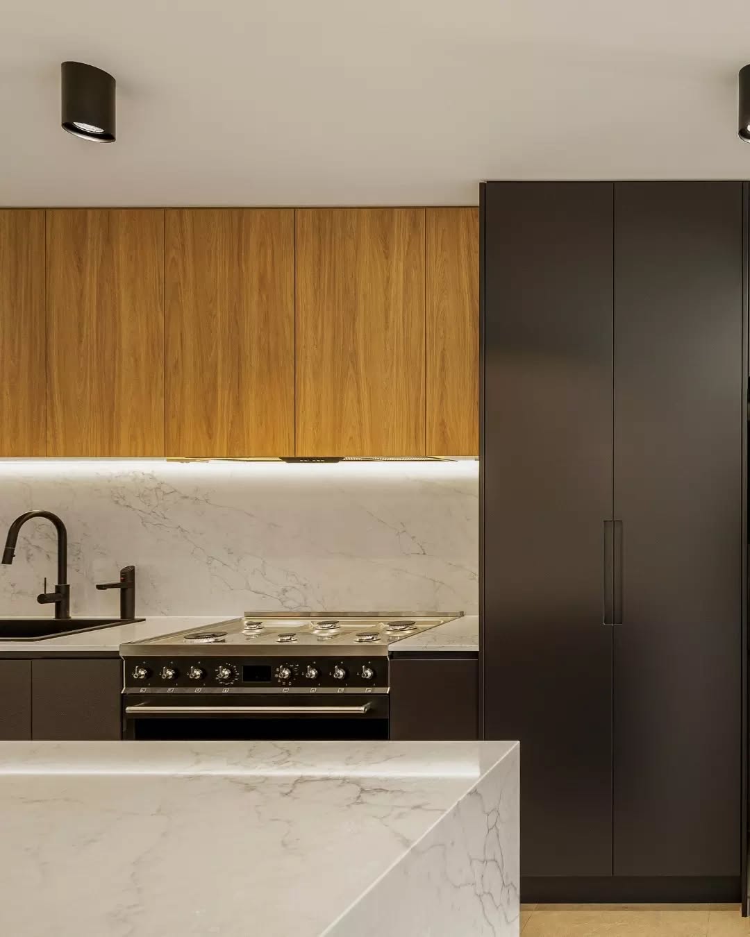 The rear of our Stanmore Terrace renovation is where heritage character meets a modern twist.
The kitchen is a standout feature, with a mix of black and warm timber cabinetry, accented by strip lighting, a large marble island bench and matching splashback.