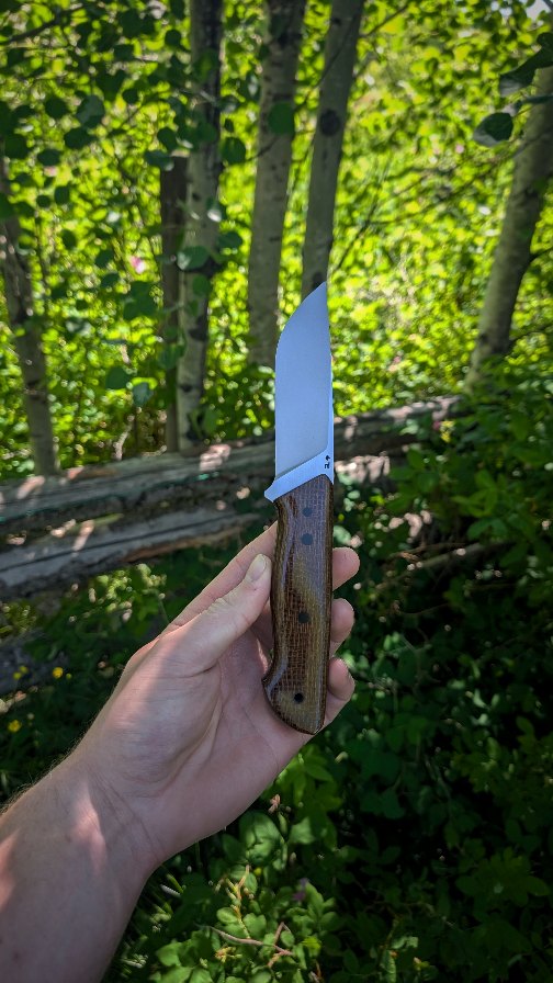 Sometimes knife making is about having fun, and learning how new prototypes feel. This Derecho model is the first of its kind in my making career. My handles have always been relatively slim and nimble for ease of carry and work. However, with this piece I wanted to make a design with a handle that completely filled out your hand. Now maybe it's because I'm not used to it, or there are slight tweaks I need to make to make it 100% perfect.
The main change is the small guard, with such a small guard, I'm considering either extending the handle all the way down the guard, or lengthening the guard itself. With a small guard, it does give you the "catch" I'm used to, which prevents your hand sliding up the blade. Now puukko knives, and other pieces don't have any guard at all, so maybe it's just a me thing!? I'd love to hear your thoughts.
Just because it's made for use doesn't mean it can't be beautiful.
Statistics.
Style: Deracho
Steel: NitroV
HRc: ≈62
Overall length: 9.5"
Blade length: 4.125"
Cutting edge: 4"
Stock: ⅛"
Handle: Burlap micarta
Liner: G10 and canvas micarta
Pins: G10
Tube: G10
As always, every step from profiling, to heat treat, to polishing, to leather work is all done myself in Northern BC, Canada.
Go off the edge of your trail