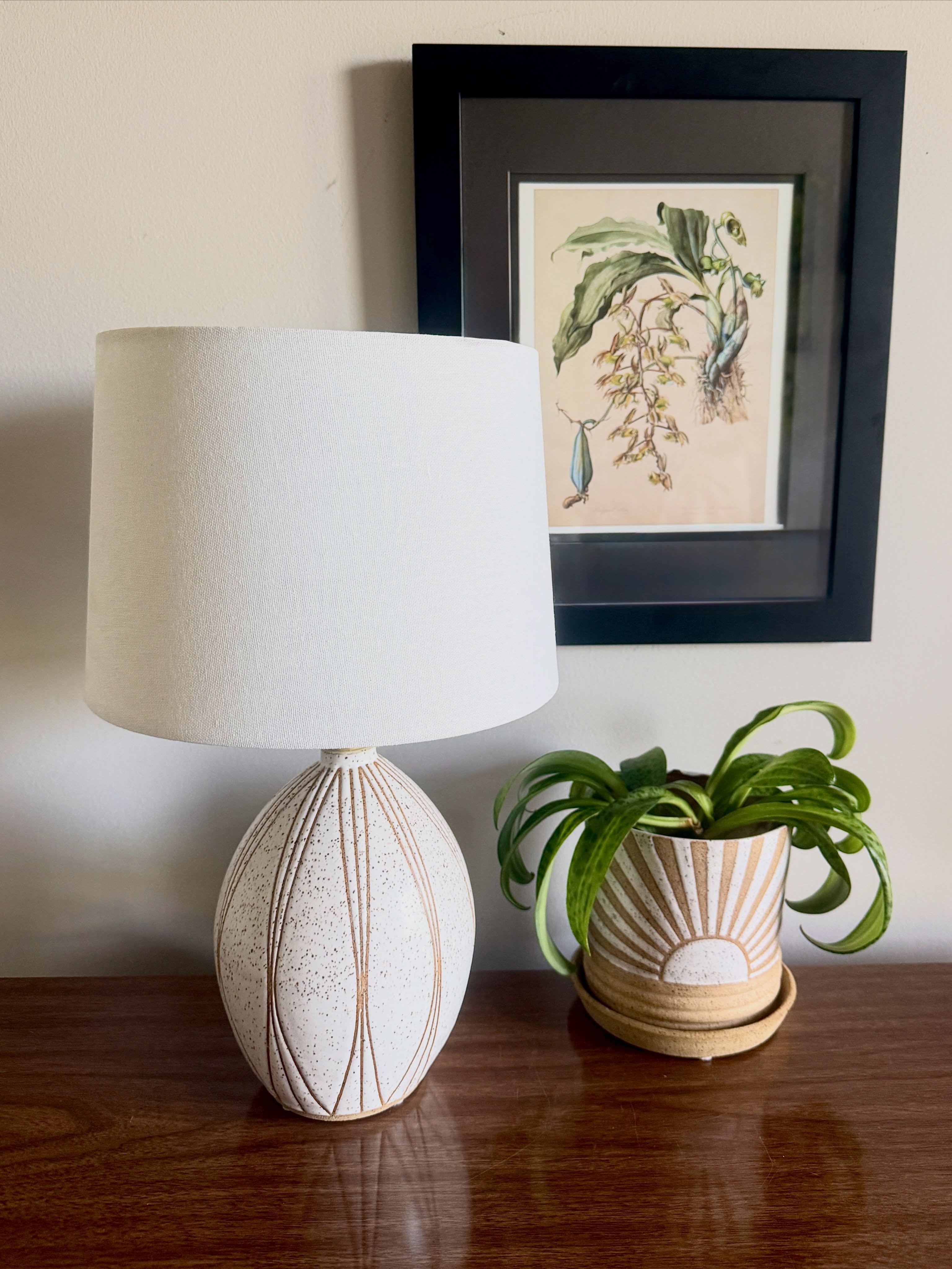 A closer look at this art deco inspired lamp 💡 Perfect for adding a warm glow to your bedroom, office, or cozy nook in your living space.
The ceramic lamp base is thrown on the wheel, and then I hand tape the design with 1/16 inch masking tape. It’s dipped in a satin white glaze that I make myself, and then the tape is removed before the final firing.
I assemble the lamp using brass fixtures, a cloth-covered cord, and a white hard-backed linen shade.
And, yes! I can make you a matching set!
#ceramics #handmadelamp #homedecor #boho