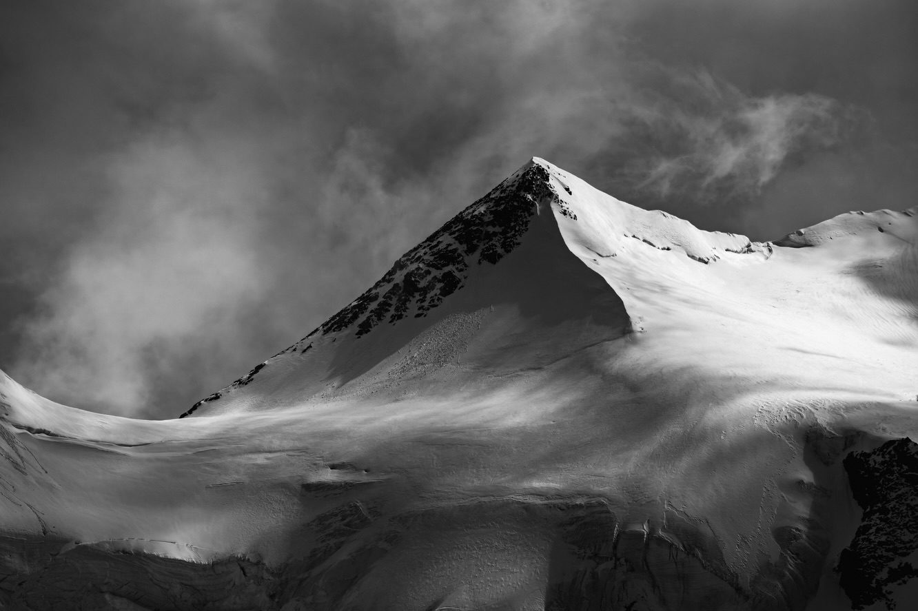 A Window Back in Time
Returning to the Swiss Alps in early June felt like stepping into another era. Although last winter was far from exceptionally snowy, the remaining snowpack was still enough to blanket many glaciers beneath a smooth white layer. Their familiar crevasses and intricate textures disappeared beneath flowing forms, transforming the landscape into something almost timeless.
For a brief moment, it became easier to imagine how these mountains may have looked decades ago, when glaciers reached much farther into the valleys and snow lingered well into summer.
Of course, I know this is only a temporary impression. Within a few weeks, almost all of the snow was gone, exposing the glacier beneath and revealing a landscape that continues to change year after year.
What fascinates me is how differently the same place can feel. Late last summer I photographed exposed ice with its countless lines, textures and shades of blue. This June, those same glaciers became vast, sculptural canvases, where passing clouds painted light and shadow across untouched snow.
These photographs have become part of my ongoing long-term project, Lights, Shadows, and Glaciers, a body of work exploring the ever-changing relationship between glaciers, weather and light in the Swiss Alps.
Perhaps photography cannot preserve the glaciers themselves. But it can preserve these fleeting moments, when light, weather and landscape come together in ways that may never be repeated.
