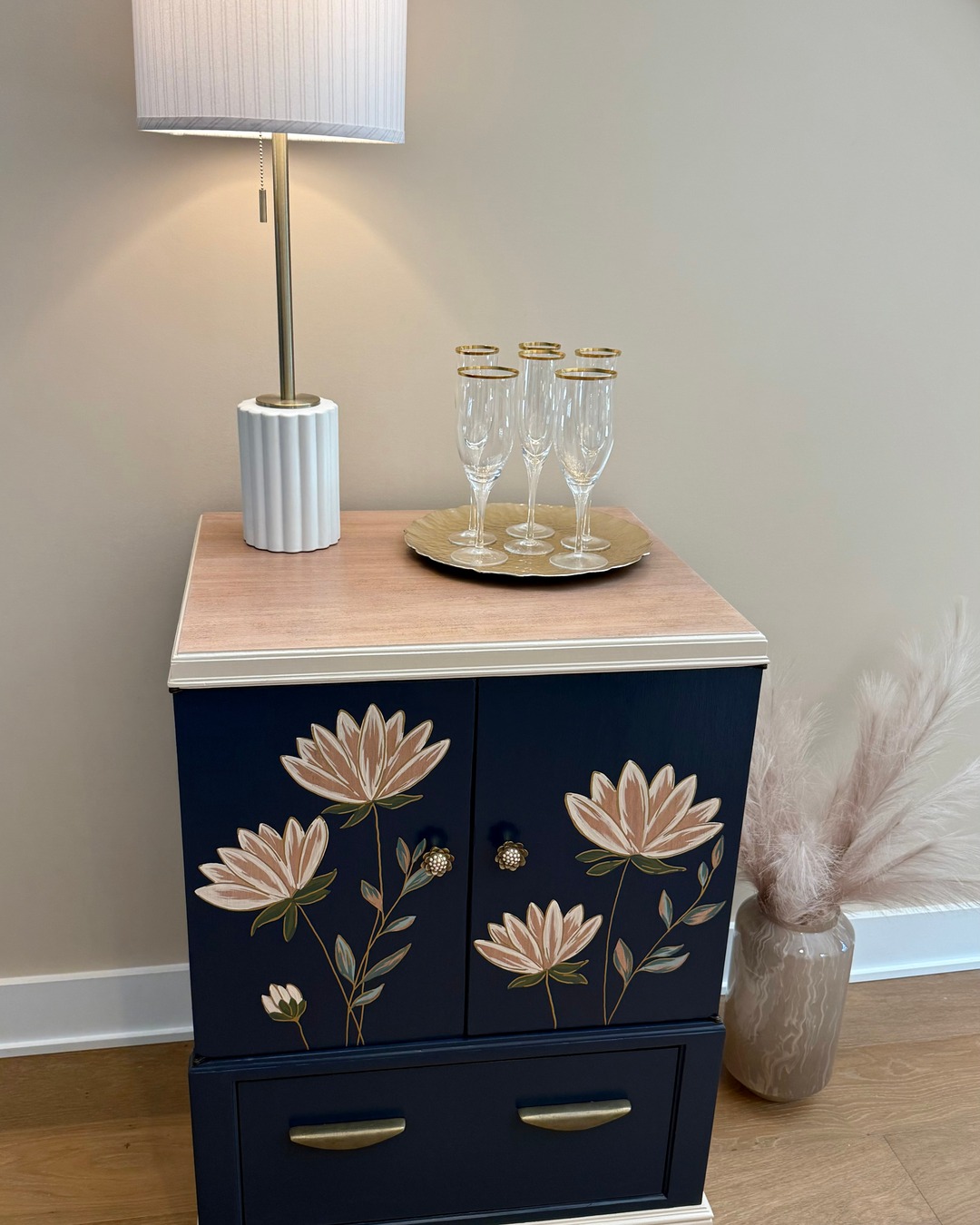 She's a little showstopper. Our Navy Floral Vintage TV Cabinet started life holding a television, but we gave her a whole new chapter — deep navy swaths the body, soft cream and whitewashed mahogany grace the top, and we hand-painted modern florals right onto the original doors. Open them up and there's coordinating floral wallpaper inside, plus we added a drawer below for extra storage. At 28"W x 21.5"D x 37"H, she's the perfect size for a nightstand, entryway, or anywhere that needs a conversation piece. She's $475 and coming with us to Vintage Market Days in Myrtle Beach, October 2–4! DM us to hold her for booth pickup. @vintagemarketdayscarolinas #vintagemarketdays #twopoppiesdesign #paintedfurniture #floraldecor