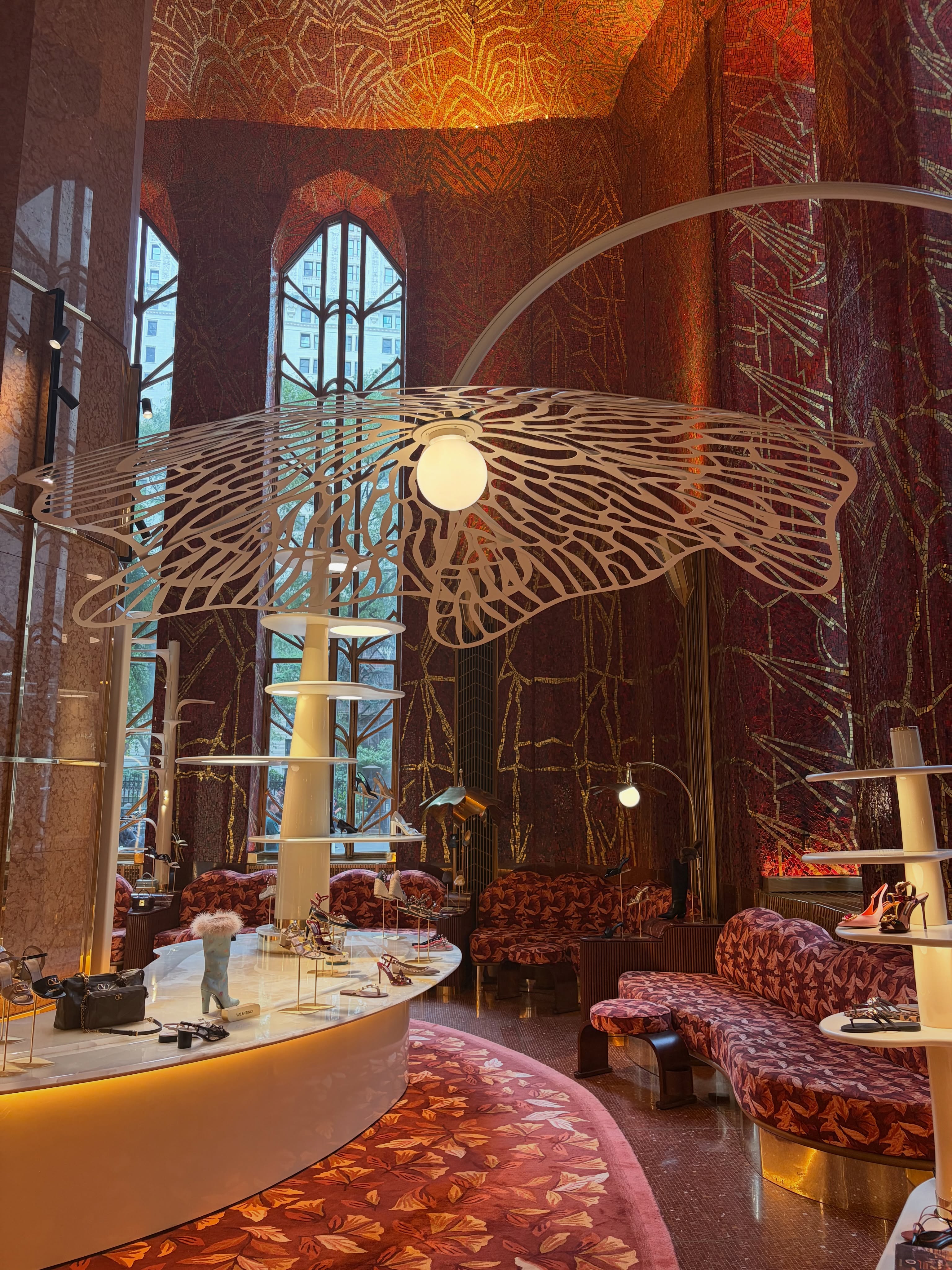 Some retail spaces are designed to become landmarks.
At Printemps New York, the spectacular Red Room dates back to 1931. Originally designed by artist Hildreth Meière, its soaring walls are covered in red and gold mosaics - a protected Art Deco interior now opened to the public through retail.
Rather than competing with the architecture, Laura Gonzalez chose to work with it. At its centre, a monumental metallic tree rises beneath the mosaics, transforming the historic room into an unexpected setting for footwear.
The contrast is striking: heritage architecture, contemporary scenography and product all sharing the same stage.